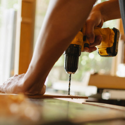 DIYA person uses a yellow cordless drill on a wooden plank in a well-lit workshop. The focus is on precision and craftsmanship, suggesting a diligent mood.